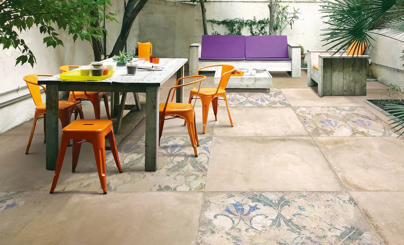 Esterno di una casa con un albero e piante verdi, pavimento in cotto tagina, un divano, tavolino e sedie colorati in viola e arancione