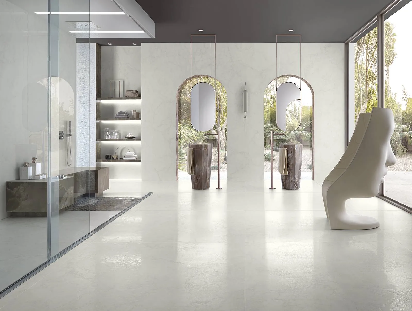 Un bagno luminoso con pavimento e rivestimento Tagina Mystery effetto marmo. 2 finestre si aprono su 2 lavabo e una sedia a forma di testa e' a lato del bagno.