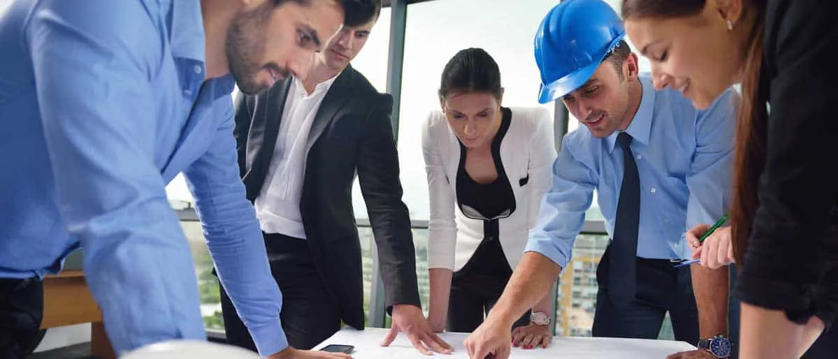 Gruppo di professionisti, uomini e donne, raccolti intorno ad un progetto. Una delle persone indossa un casco blu e indica qualcosa sul progetto